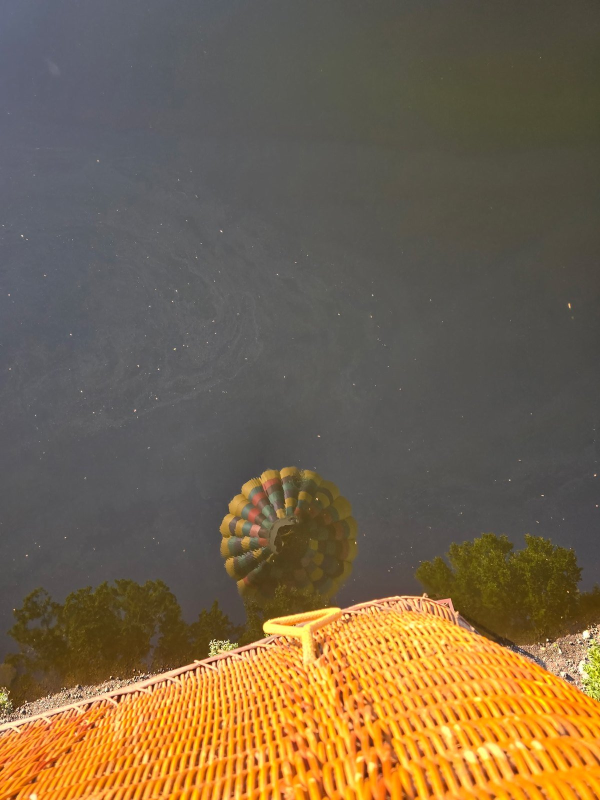Colorful hot air balloon reflected in a dark pond below the wicker basket