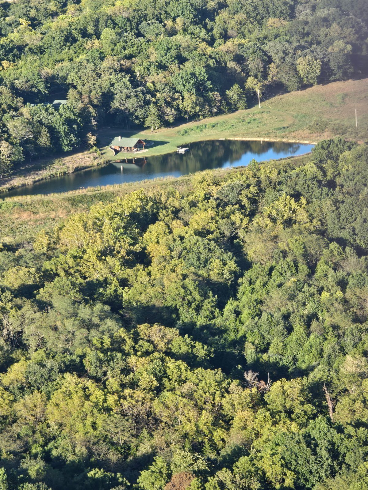 Cabin beside a lake surrounded by trees, seen from a hot air balloon