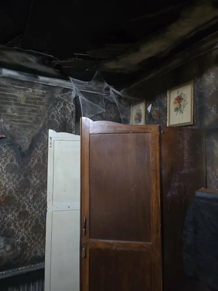 Charred ceiling, antique wardrobe and framed flower prints inside the Burn escape room