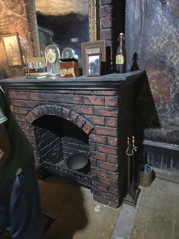Old brick fireplace with glass-domed clock and vintage photos on the mantel in the Burn escape room