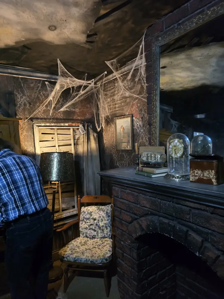 Floral rocking chair, lamp and cobwebs beside the mantel in the Burn escape room